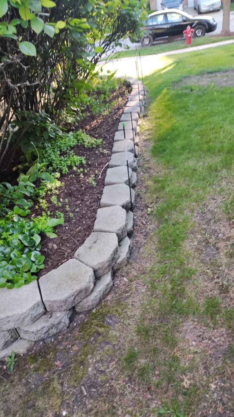 Stacked stone edging curving around a mulched bed at the lawn line