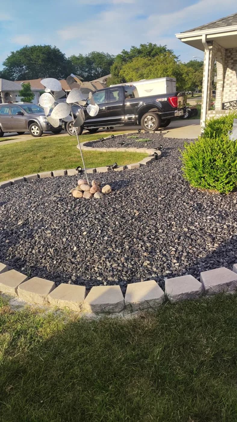 Front yard island bed filled with dark decorative stone and edged in pavers