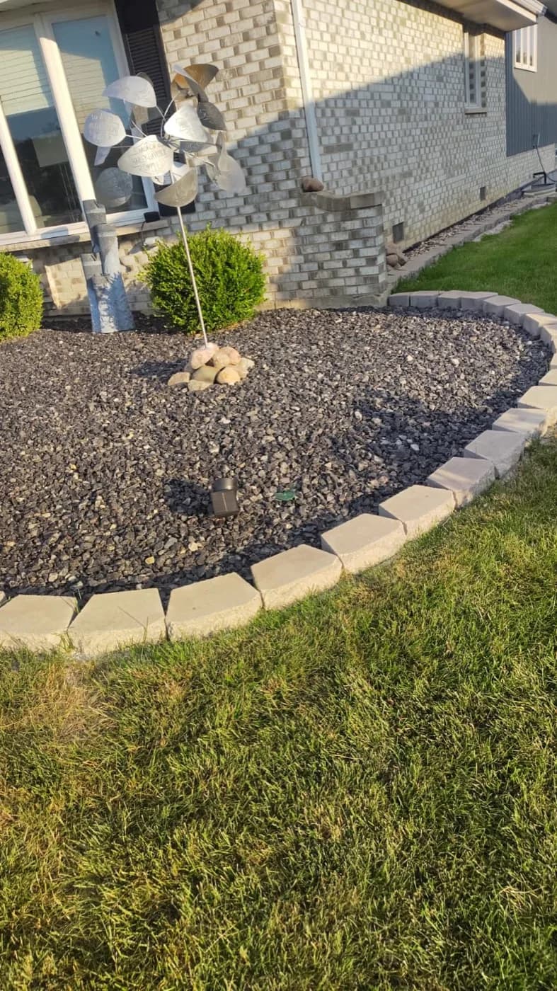 Sweeping stone mulch bed held by a tan paver border along a foundation